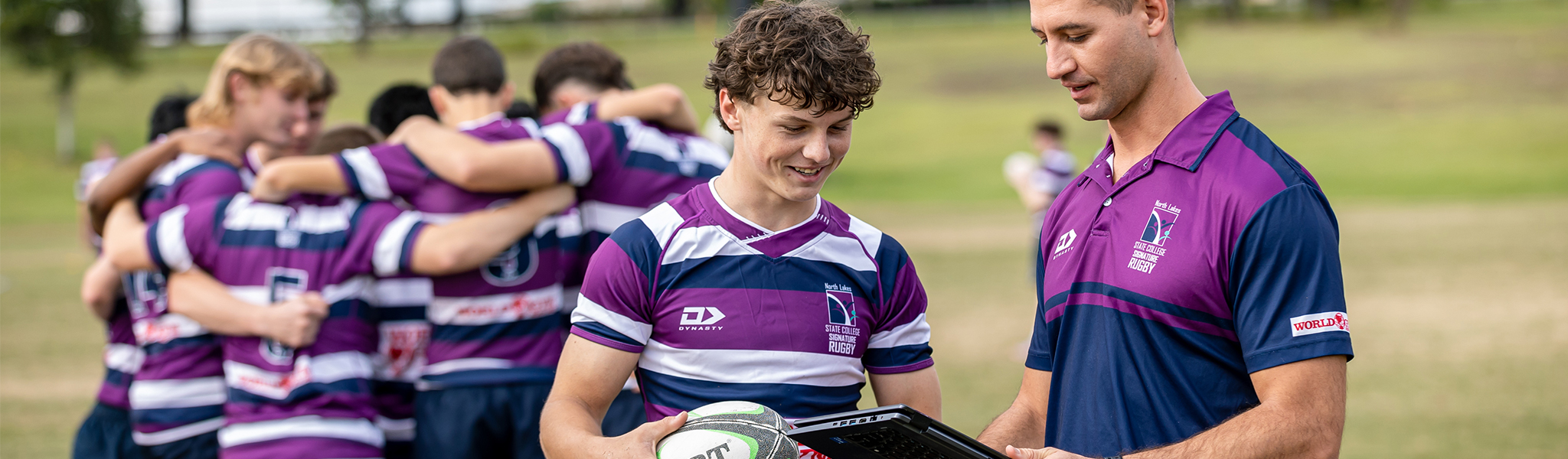 Students outdoors in sports uniforms. Staff member with a tablet.